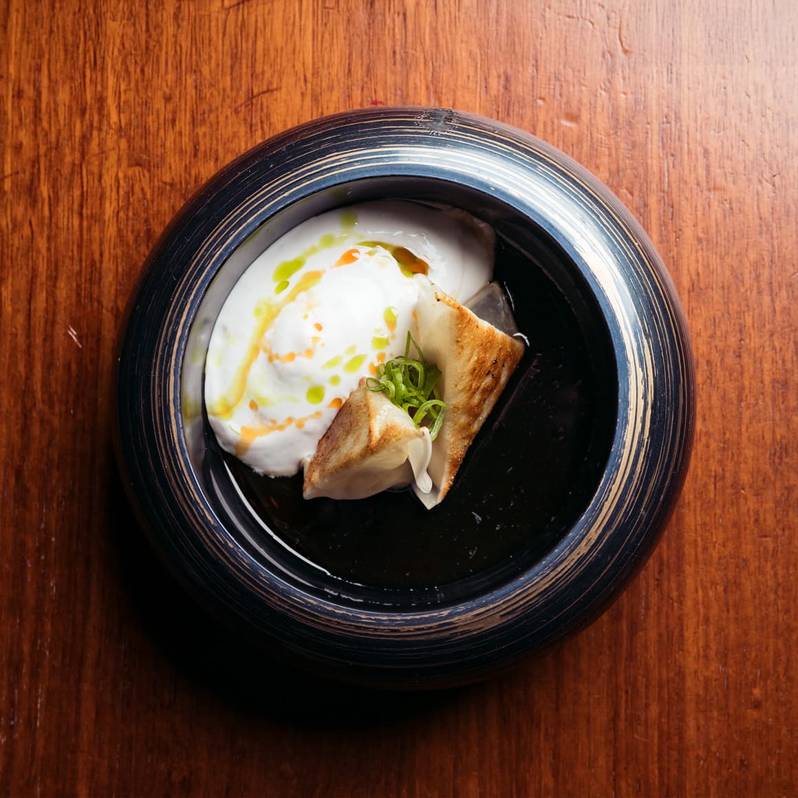 A dark plate with a dollop of creamy yogurt, topped with green garnishes and two triangular pieces of toasted bread, placed on a wooden table.